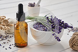 Dropper bottle of essential lavender oil, mortar of dry lavender flowers and sachets on white table