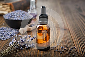 Dropper bottle of essential lavender oil. Bowl of dry lavender flowers on background