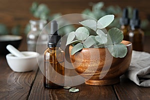 Dropper bottle of eucalyptus essential oil and wooden bowl of green eucalyptus leaves. Mortar and oil bottles on background