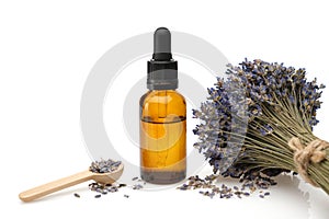 Dropper bottle of lavender essential oil or aromatic flower water, wooden spoon of dry petals and bunch of dried lavender flowers