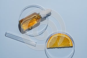 Dropper bottle with orange serum with vitamin C in a petri dish next to orange slice and a test tube. Laboratory