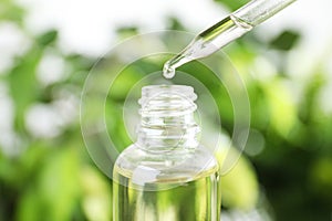 Dropper with essential oil over bottle against blurred background