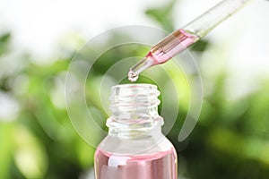 Dropper with essential oil over bottle against blurred background