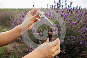 Dropper with lavender essential oil over a bottle in a blooming field