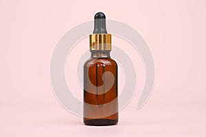 Dropping essential oil into glass bottle, bottle of hyaluronic acid with pipette isolated on pink background with copy space.