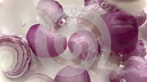 Dropping few cut red onions in sparkling water as it creates bubbles and a few splashes