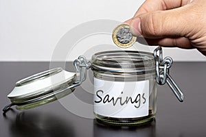 Dropping one pound coin into jar for Savings