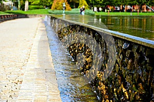 Dropping pool water on rough natural stone wall in public park.