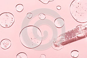 Drops of anti-aging emulsion and glass pipette on light pink