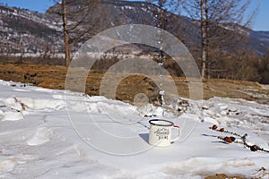 Drops of clean water from Lake Baikal are splashed from a metal aluminum mug on the snow on a picturesque mountain background.