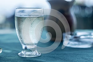 Drops of condensation on the misted glass of a glass with a transparent liquid on the table with a blue tablecloth and a blurred b