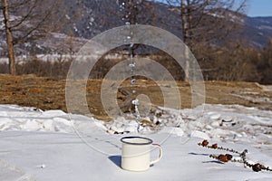 Drops of drinking water from Lake Baikal are splashed from a metal aluminum mug with empty space for text on the snow.