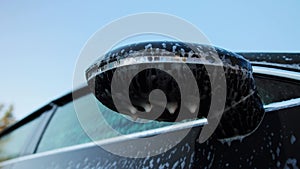 drops of foam with water drip from the side rear view mirror of a car, close-up. Car wash in nature, close-up. Slow