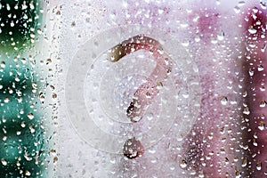 Drops of morning summer rain on a fogged window with a question mark drawn on a blurred background of nature in the daytime.