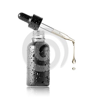 Drops of oil dripping from a cosmetic pipette isolated on a white background. Black bottle with cosmetic oil close up