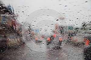 Drops Of Rain Drizzle on the glass windshield in the evening. street in the heavy rain. Bokeh Tail light and Traffic lights in cit