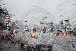 Drops Of Rain Drizzle on the glass windshield in the evening. street in the heavy rain. Bokeh Tail light and Traffic lights in cit