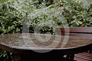 Drops of rain fall on wooden terrace in green garden outdoors. Empty wooden table against summer rain weather