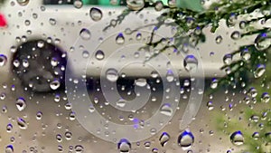 The drops of rain on the glass. In the background blurred cars. Trees move with the wind. The view through the window