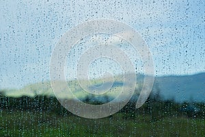Drops of rain on the window; blurred mountains in the background; shallow depth of field