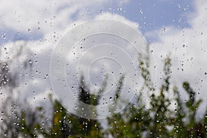 Drops of rain on the window; blurred trees and clouds in the background; sunshine after the rain, shallow depth of field