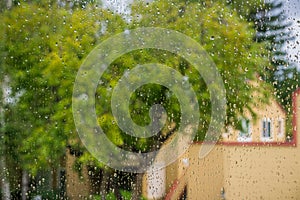 Drops of rain on the window, blurred trees and house in the background