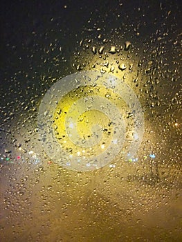 Drops of rain on window at night. Rainy and night city behind  glass. Tears of the sky flow down  transparent wall. Bead drops