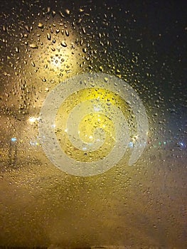 Drops of rain on window at night. Rainy and night city behind  glass. Tears of the sky flow down  transparent wall. Bead drops