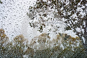 Drops of rain on the windshield; cloudy sky and autumn colored trees in the background