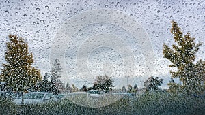 Drops of rain on the windshield; cloudy sky and autumn colored trees in the background