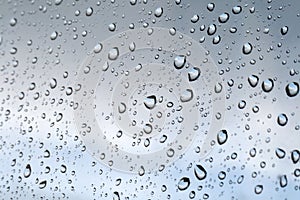 Drops of water on the glass window against a blurred blue and gray sky background on a rainy autumn day. Selective focus