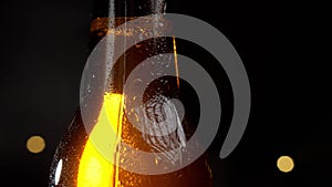 Drops of water slowly flow down a cold bottle of beer. On a black background