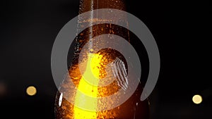 Drops of water slowly flow down a cold bottle of beer. On a black background