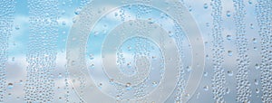 Drops water on window for wallpaper design. Blue cloudy sky backdrop. Spotted abstract texture background. Spring wet