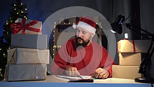 Dropshipping owner male Hindu Santa Claus works at night in his home office, with a boxes before shipping to a customer