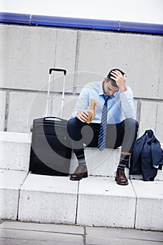 Drowing his sorrows. A young businessman sitting outdoors and drinking while looking dejected.
