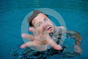 Drowning caucasian man in swimming pool asking for help. He stretching his hands in fear.