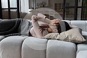 Drowsy latin woman lie on sofa hide face in palms photo