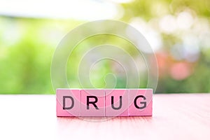 The drug word written on pink color wood block on wooden and nature background, COVID-19 concept