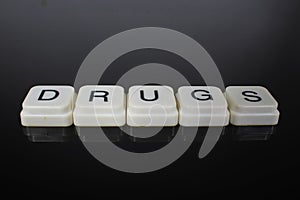 Drugs text word title caption label cover backdrop background. Alphabet letter toy blocks on black reflective background. White al