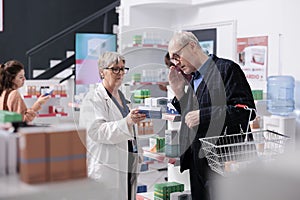 Drugstore employee helping customer with pharmaceutical treatment explaining cardiology pills leaflet