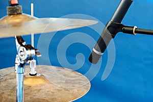 Drum cymbals and microphone are located on a blue background. Amplification and recording of the sound of musical instruments.