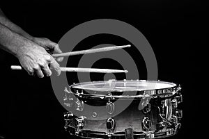 Drum sticks hitting snare drum with splashing water on black background under studio lighting. Black and white. Close up