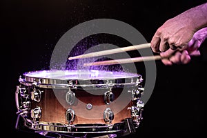 Drum sticks hitting snare drum with splashing water on black background under studio lighting