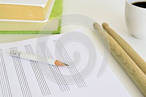 Drum sticks, a pencil and a music sheet next to some books and a cup of coffee on a desk in a classroom. Empty copy space