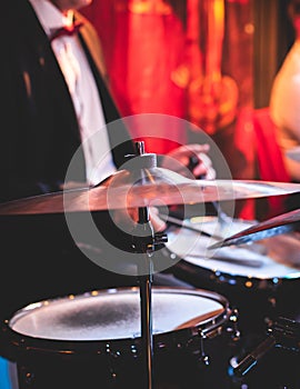 Drummer percussionist performing on a stage with drum set kit during jazz rock show performance, with band performing in the