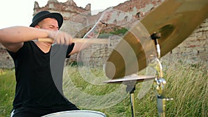 Drummer, playing drum set and cymbals, on street near a destroyed building