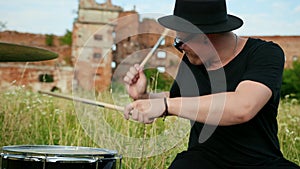 Drummer, playing drum set and cymbals, on street near a destroyed building