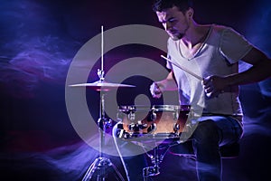 A drummer plays drums on a blue background. Beautiful special effects of light and smoke