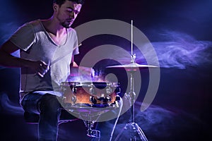 A drummer plays drums on a blue background. Beautiful special effects of light and smoke